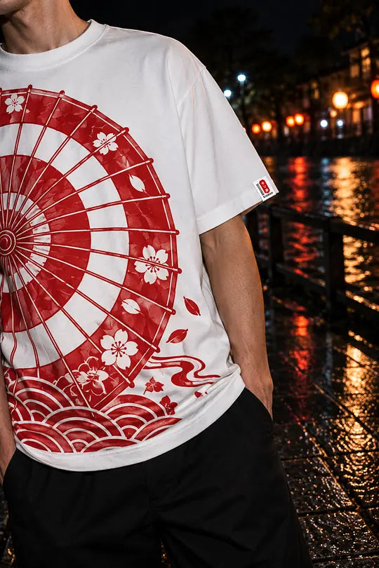 A white heavyweight tee with a large red festival-umbrella print, worn on a riverside street at night.
